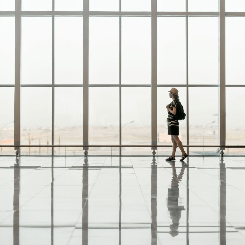 A lonely young girl walks down a huge hall with many windows