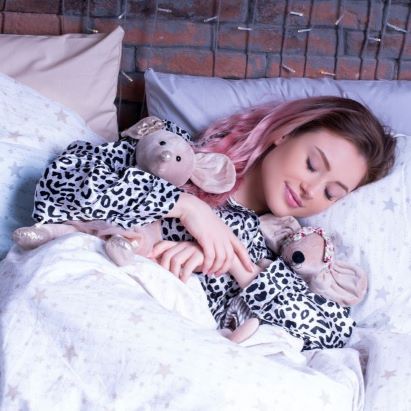 A smiling woman sleeps in bed with her toy